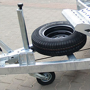 Pełnowymiarowe koło zapasowe mocowane poziomo na dyszlu nie utrudnia dostępu do koparki. Automatyczne koło podporowe zapewnia stabilne parkowanie przyczepy.